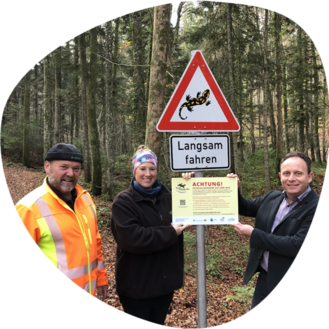 Drei Helfer stellen ein Warnschild für die Salamanderwanderung auf (Foto: Katharina Koppetsch)